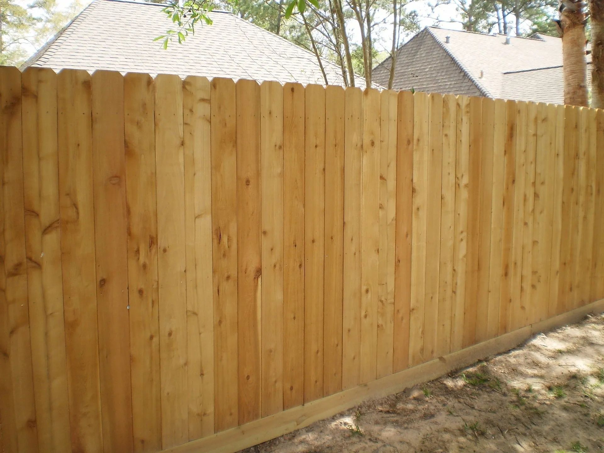 Wooden privacy fence along a yard with trees and thatched roofs visible above it