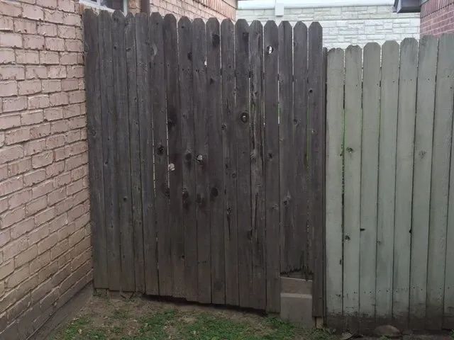 Weathered wooden gate beside a brick wall and gray fence in an alleyway