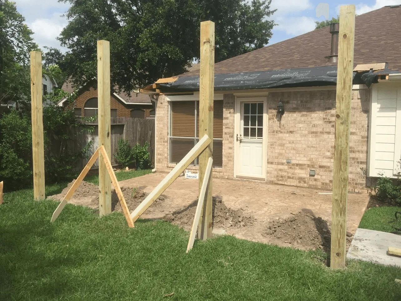 Wooden posts and braces in a backyard beside a stone house under construction