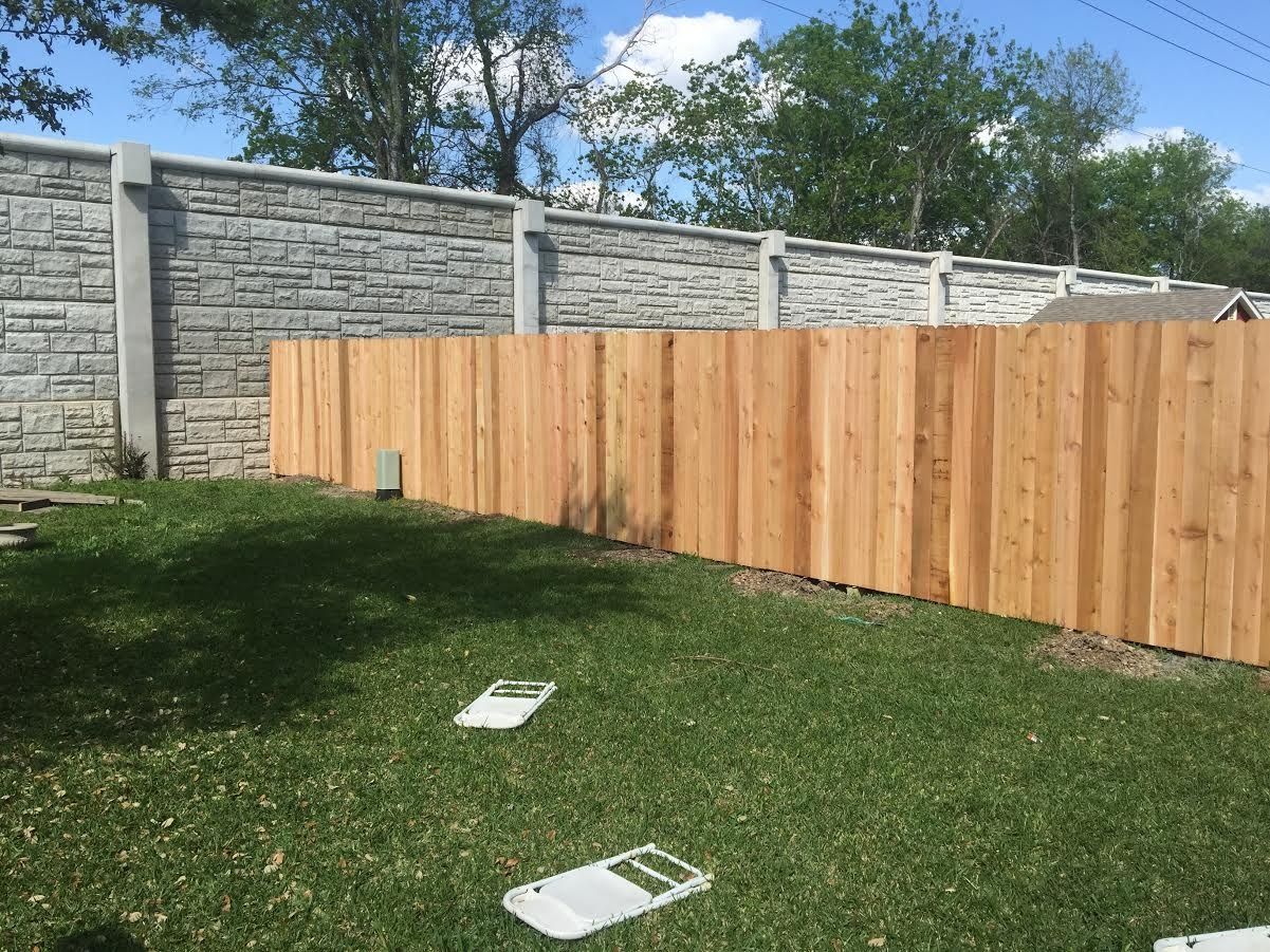 Backyard with wooden fence and concrete wall, green grass, and two white panels on the lawn