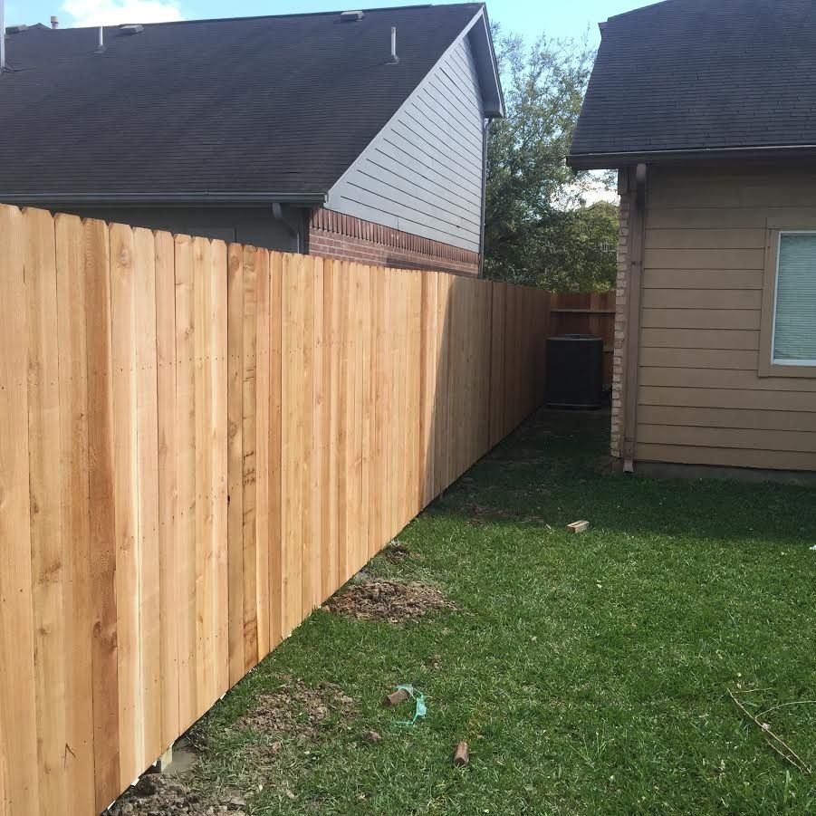 Wooden privacy fence runs alongside a grassy yard between two houses.