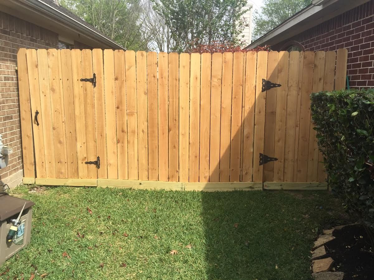 Wooden backyard fence with a central gate, bordered by grass and a hedge.