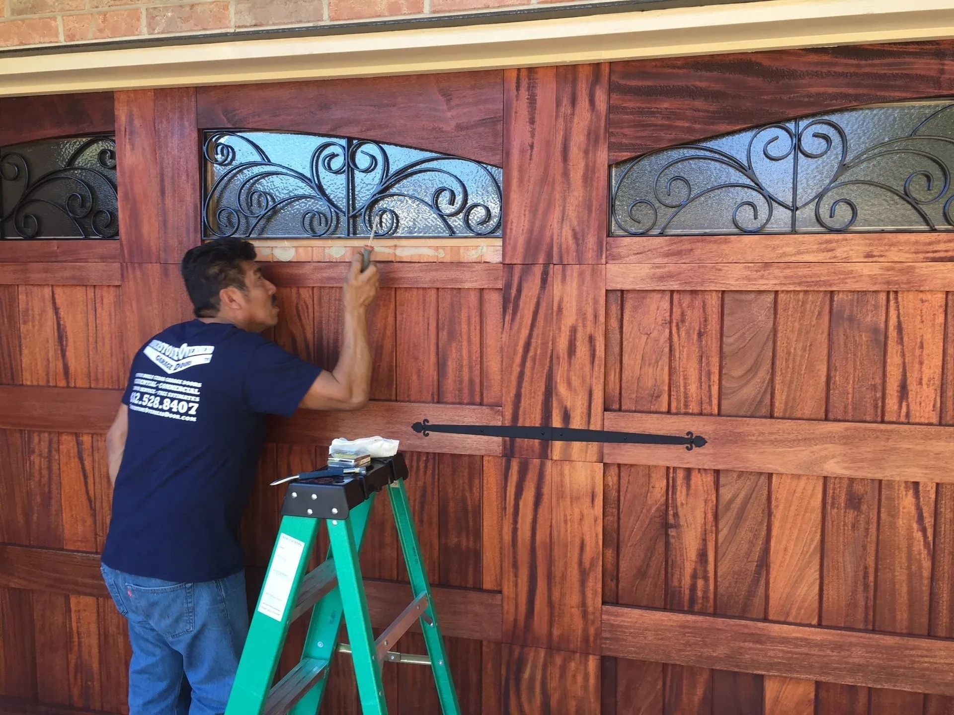 Man on teal ladder adjusting a wooden garage door with decorative glass panels