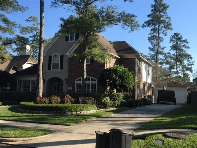 Large two-story suburban house with a driveway, garage, and tall pine trees in front