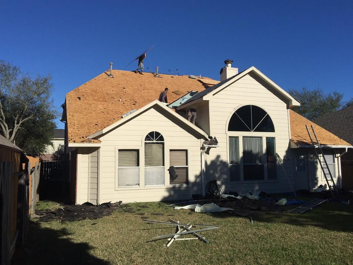 Damaged house with a partially collapsed roof and debris in the yard under a clear blue sky