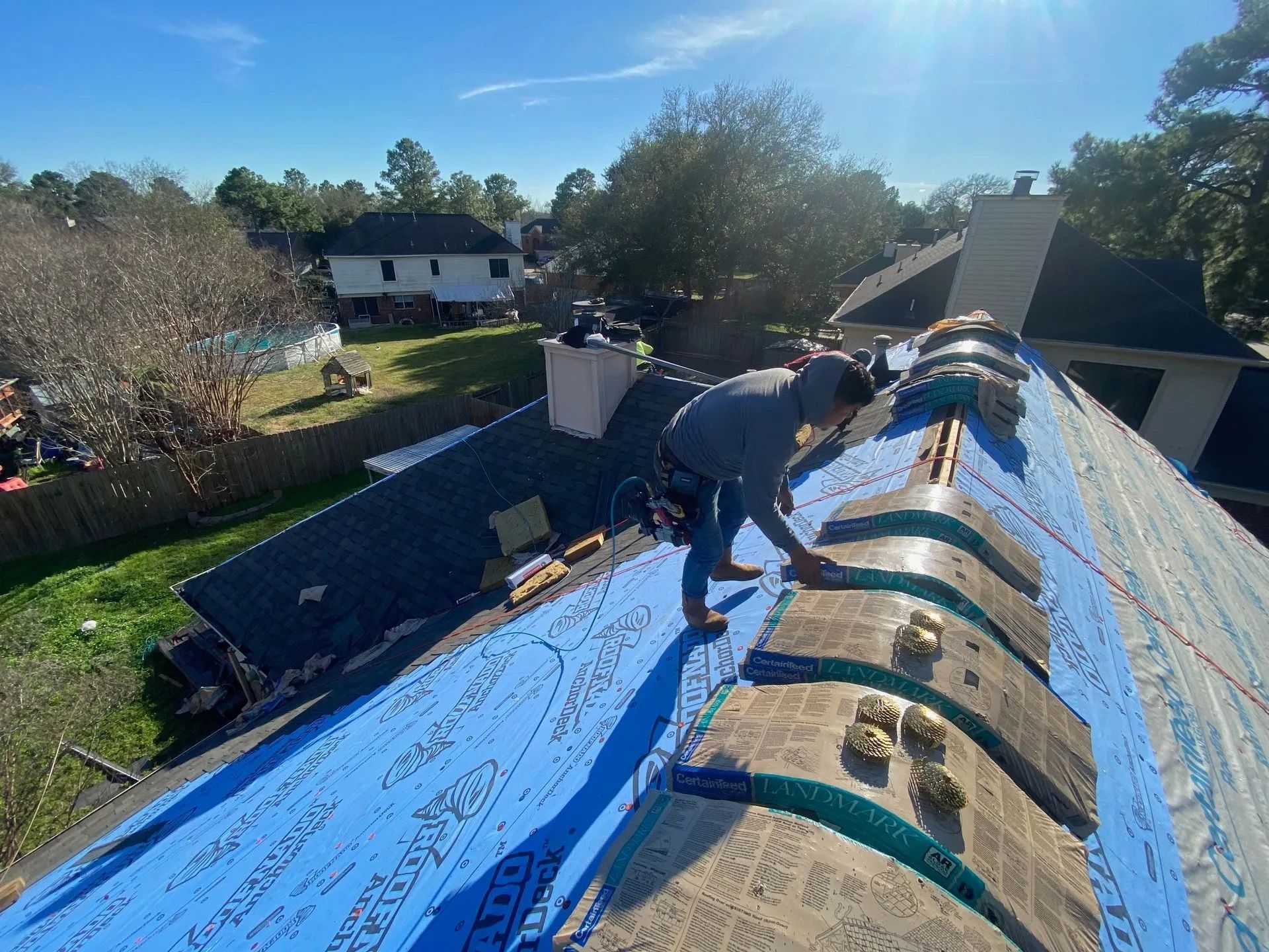 Worker installing roofing underlayment on a house roof on a sunny day