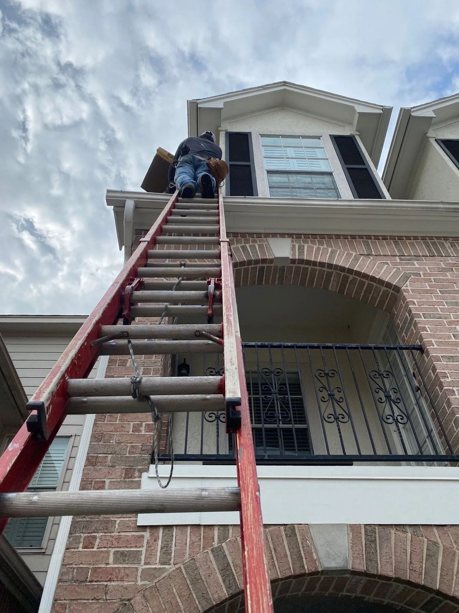 Two workers on a red ladder repairing the roof of a brick house