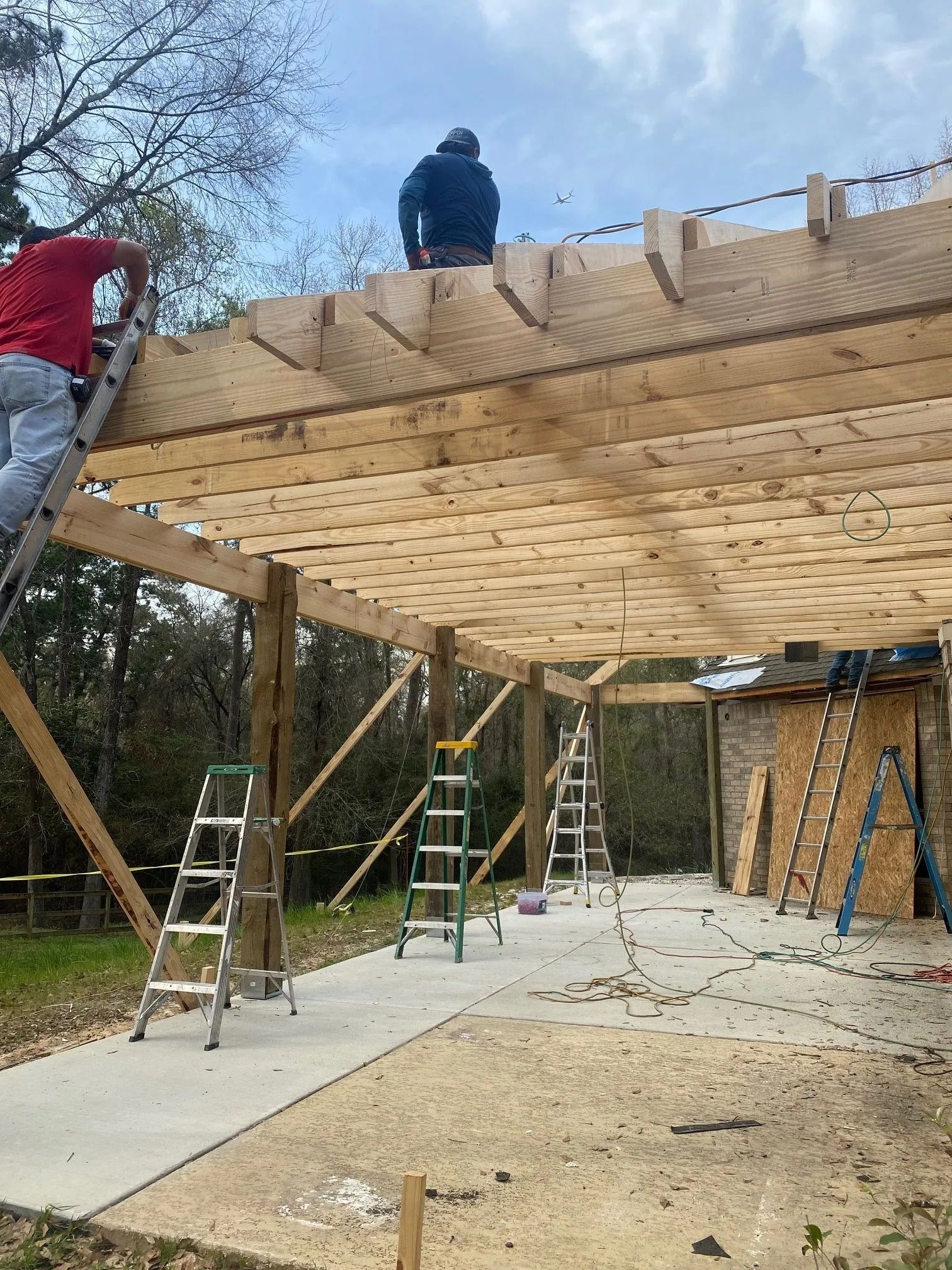 People constructing a wooden deck frame overhead, with ladders and support posts in a yard