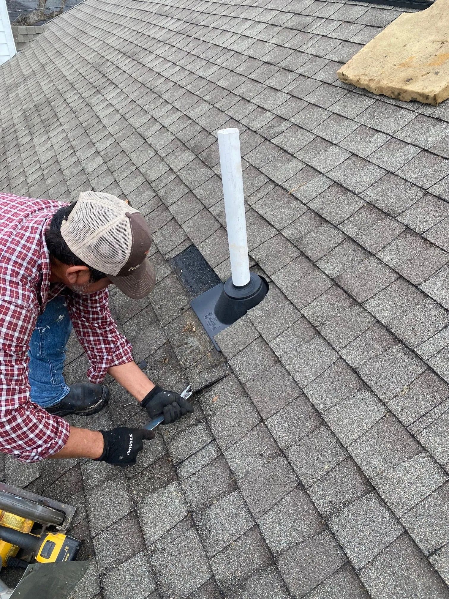 Worker installing a rooftop vent pipe on gray asphalt shingles