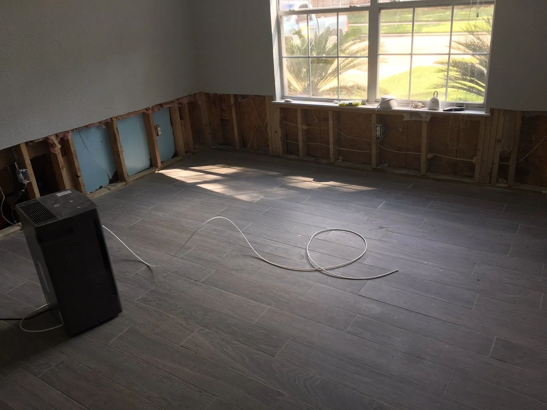 Empty room under renovation with exposed studs, dark flooring, and a window letting in sunlight.