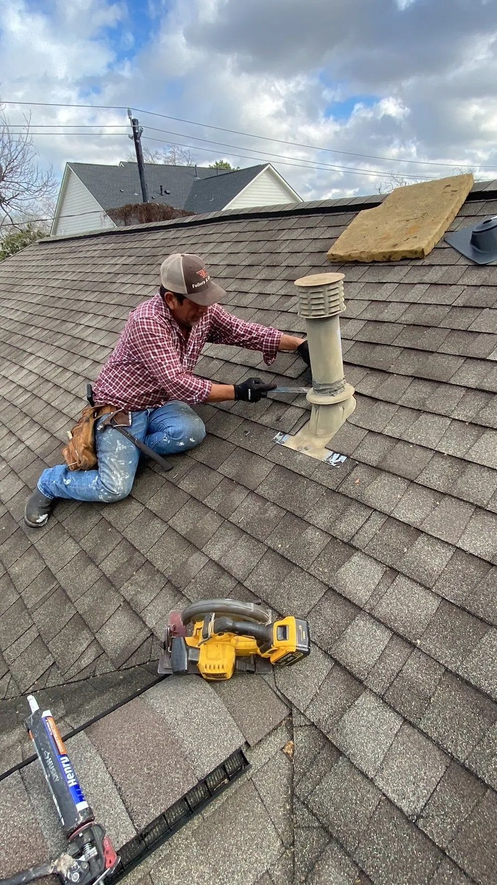 Worker installing a roof vent on a shingled roof with a drill and tools nearby