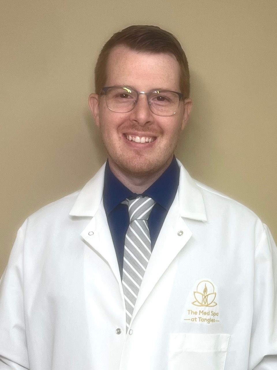 A man in a lab coat and tie is smiling for the camera