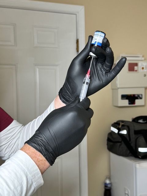 A person wearing black gloves is holding a syringe in their hand
