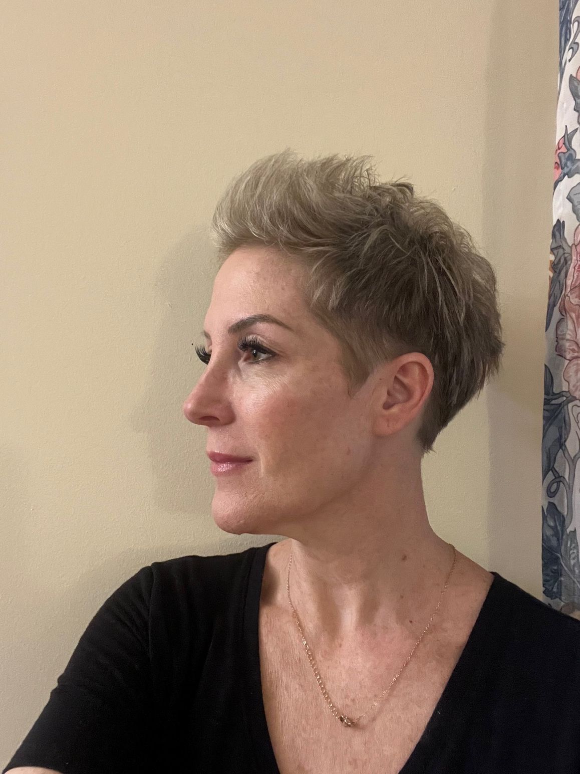 A woman with short blonde hair is wearing a black shirt and a necklace.