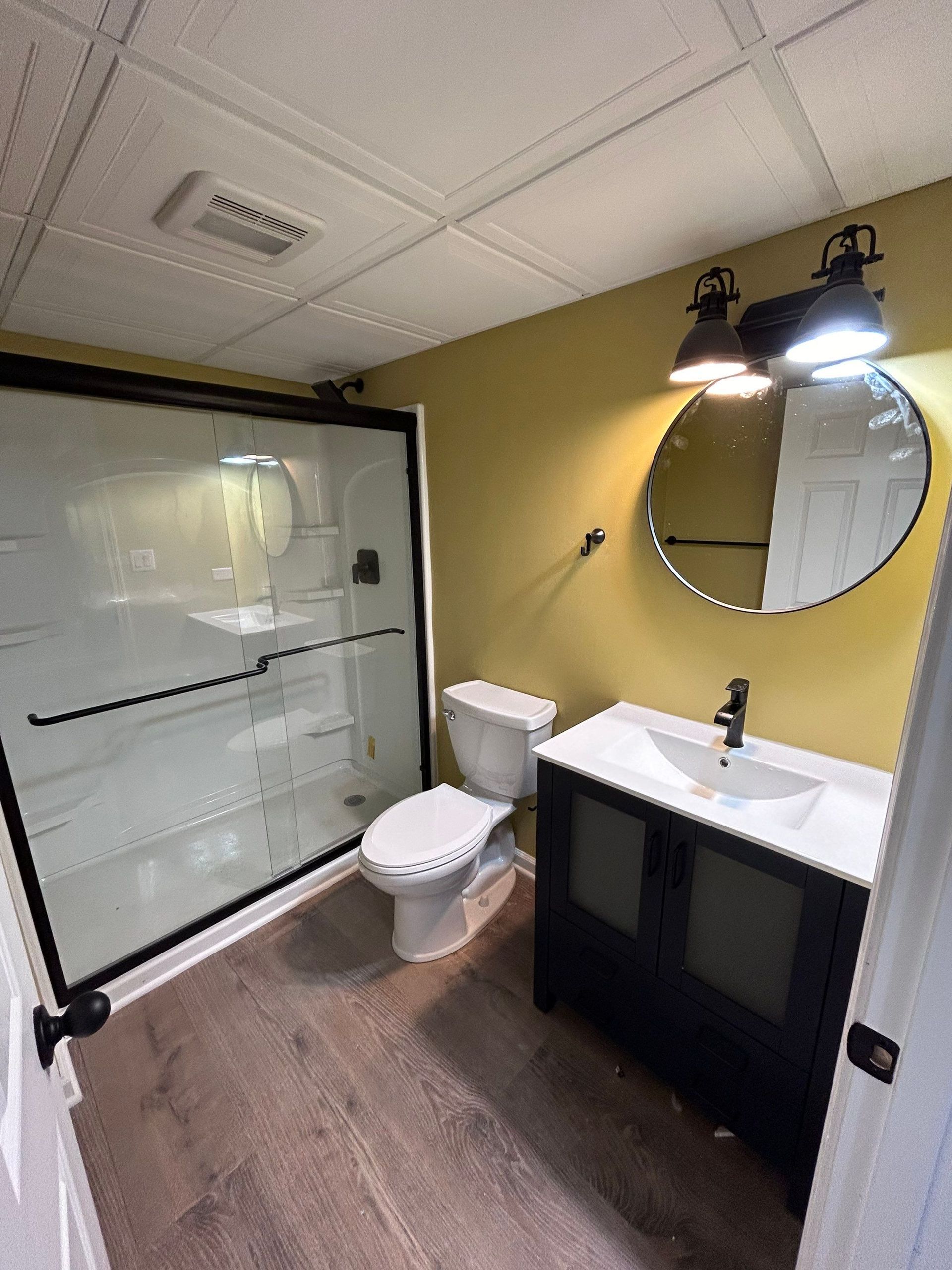 A bathroom with a toilet , sink , shower and mirror.