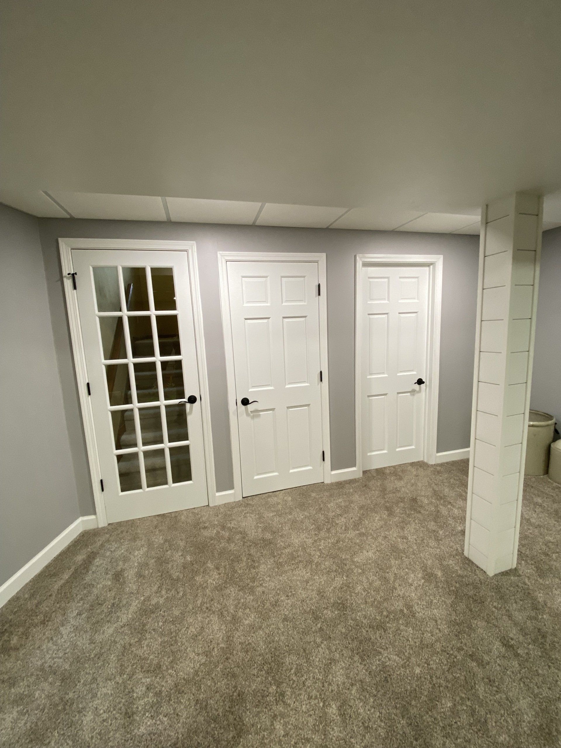 An empty basement with french doors and a pillar.