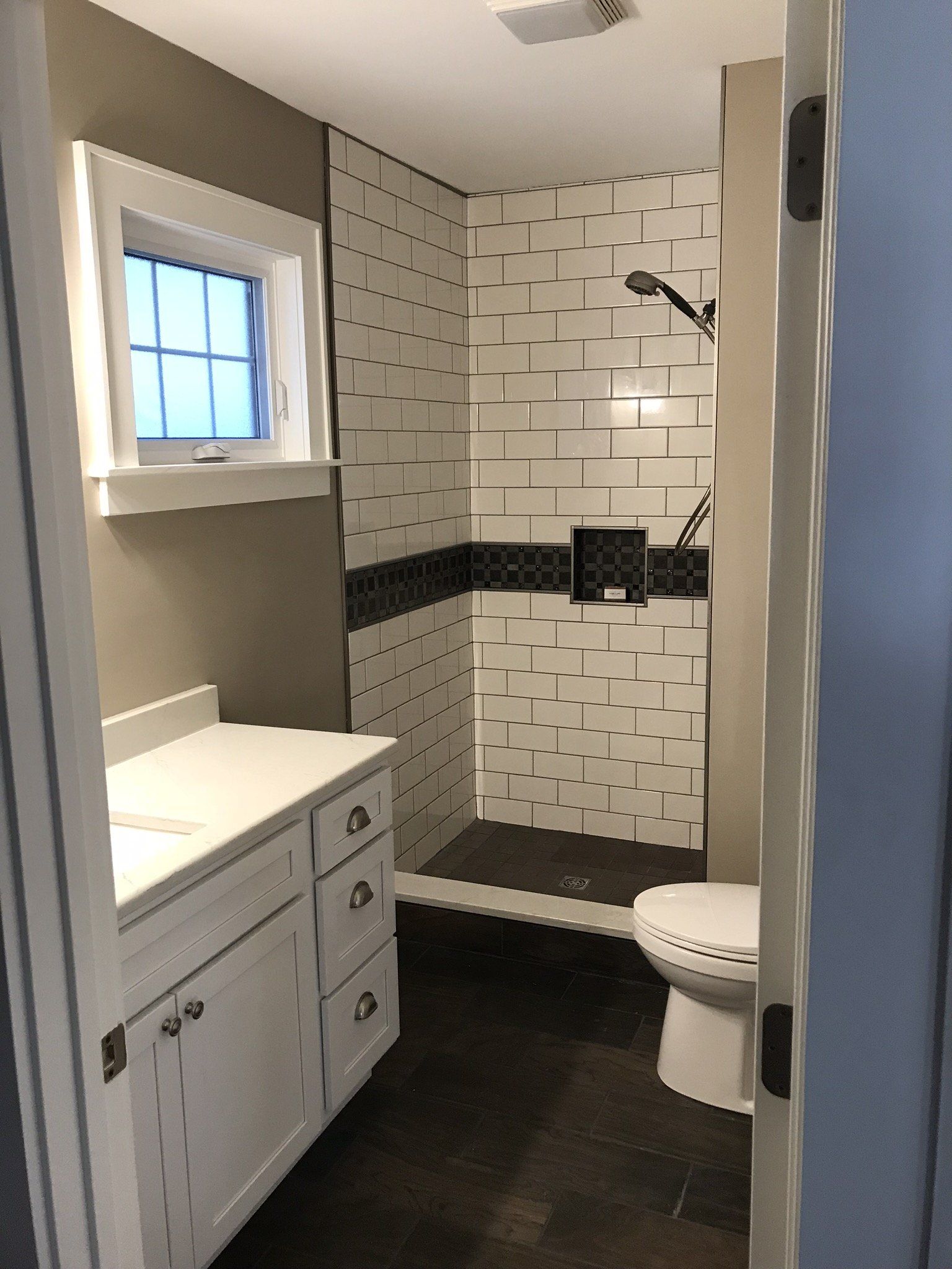 A bathroom with a toilet , sink , shower and window