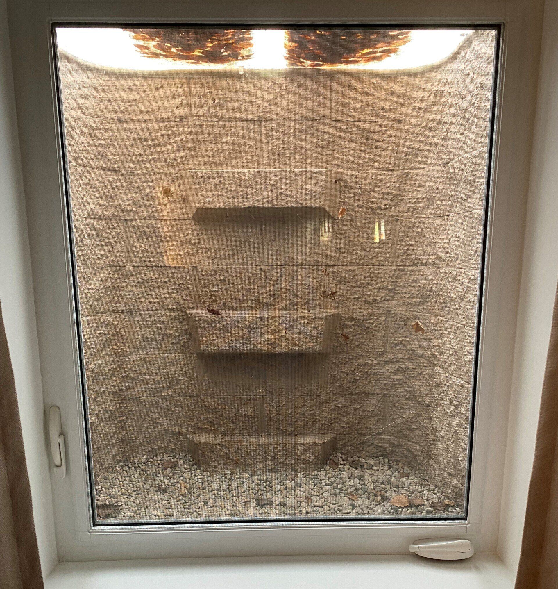 A window with a view of a stone shower stall.