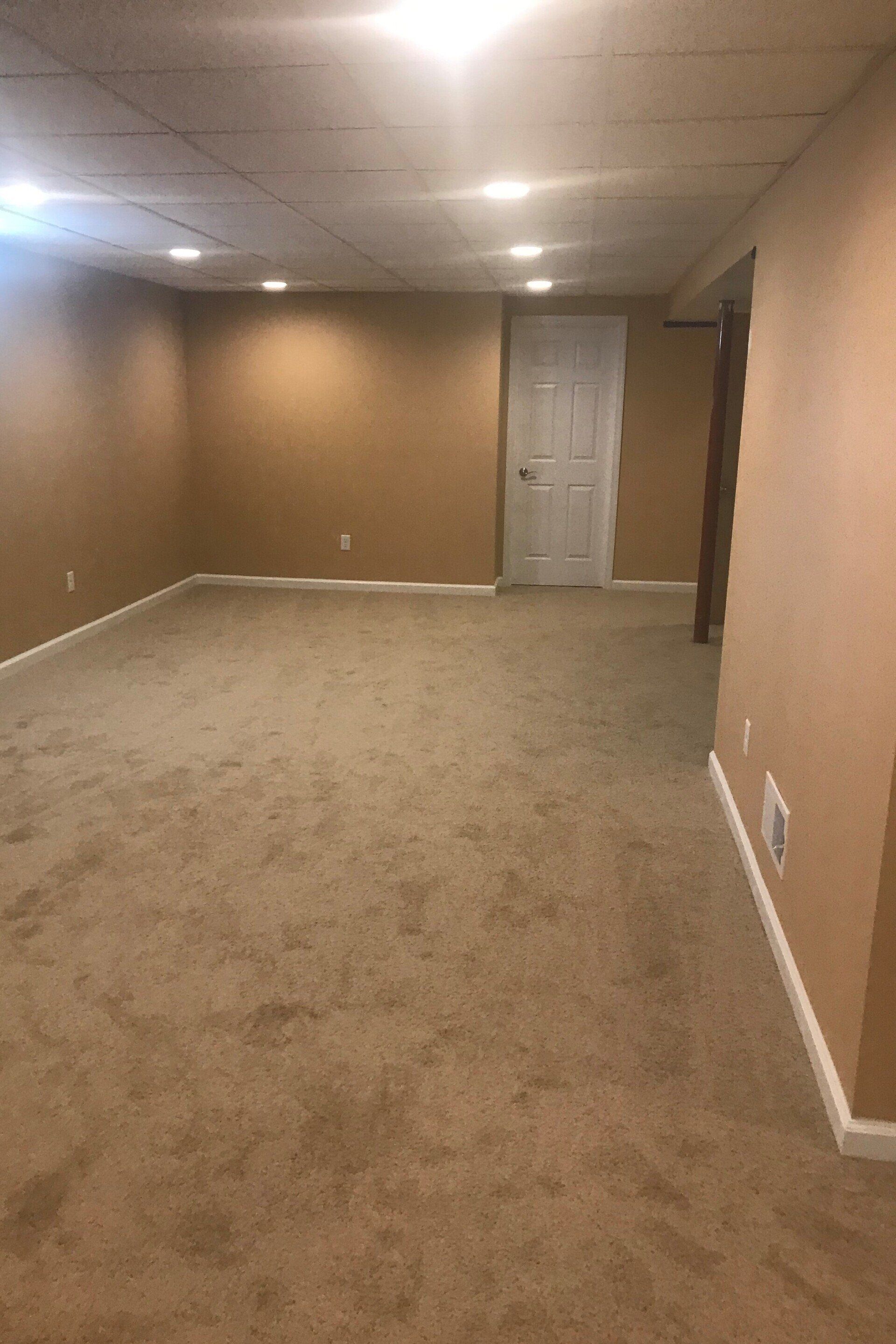 An empty basement with a carpeted floor and tan walls.