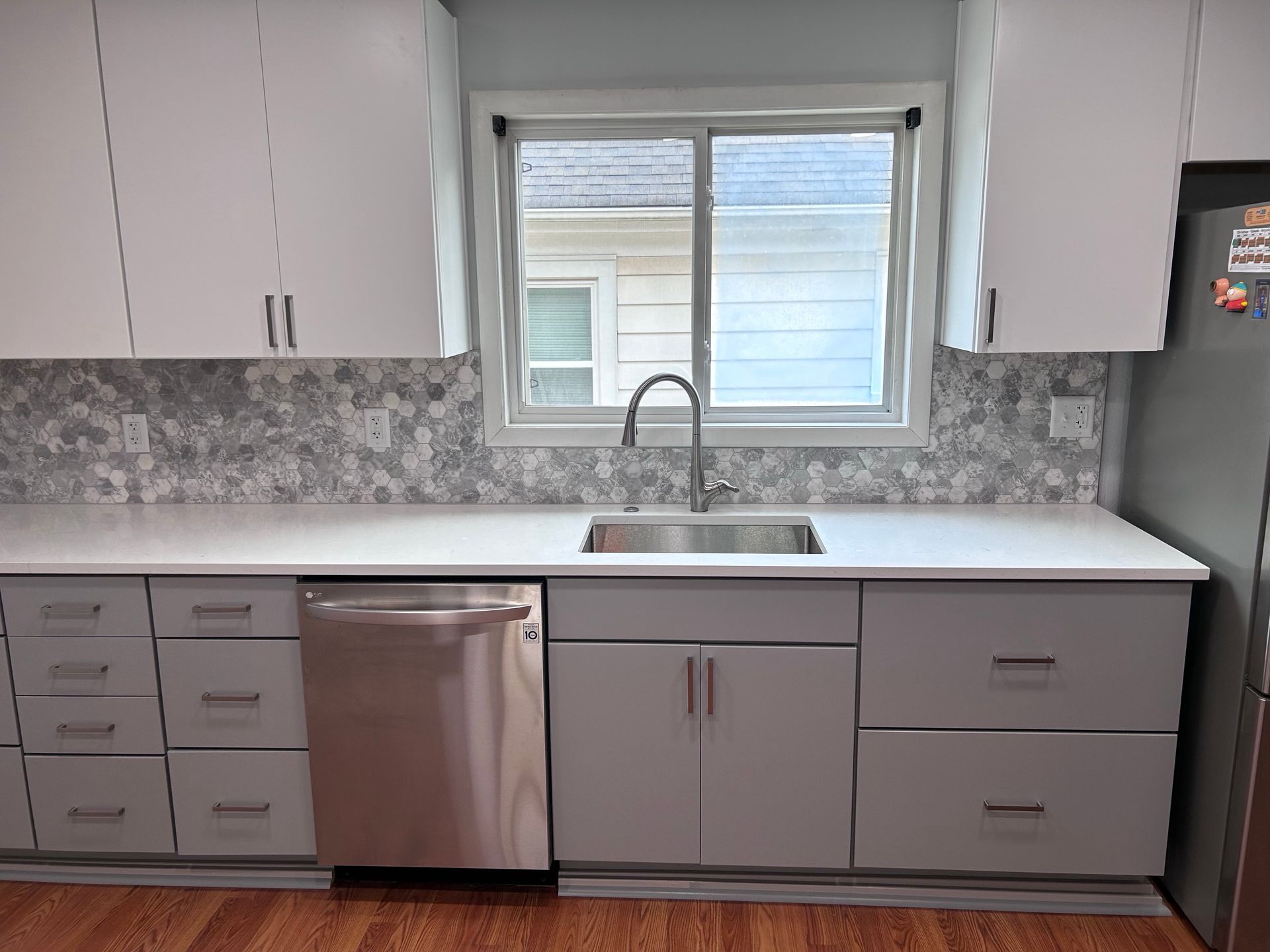 A kitchen with white cabinets , stainless steel appliances , a sink and a window.