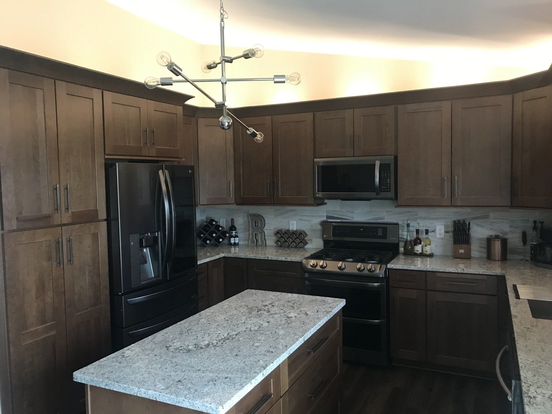 A kitchen with wooden cabinets , granite counter tops , a stove , refrigerator and microwave.