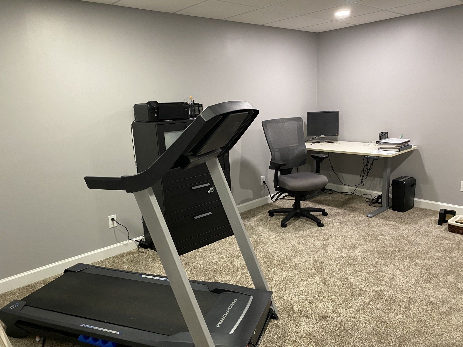 A treadmill is sitting in a room next to a desk and chair.