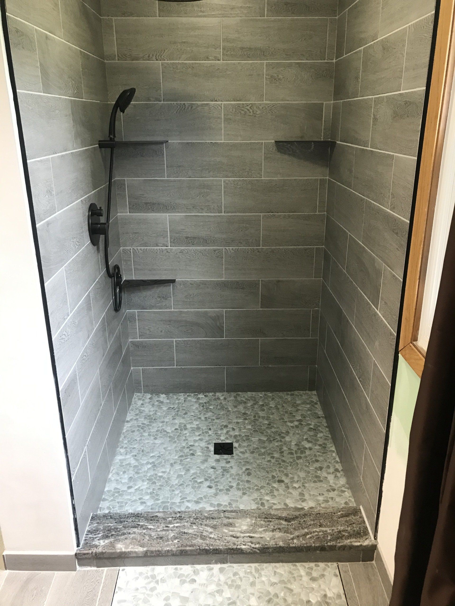 A walk in shower with a tiled floor and a black shower head.