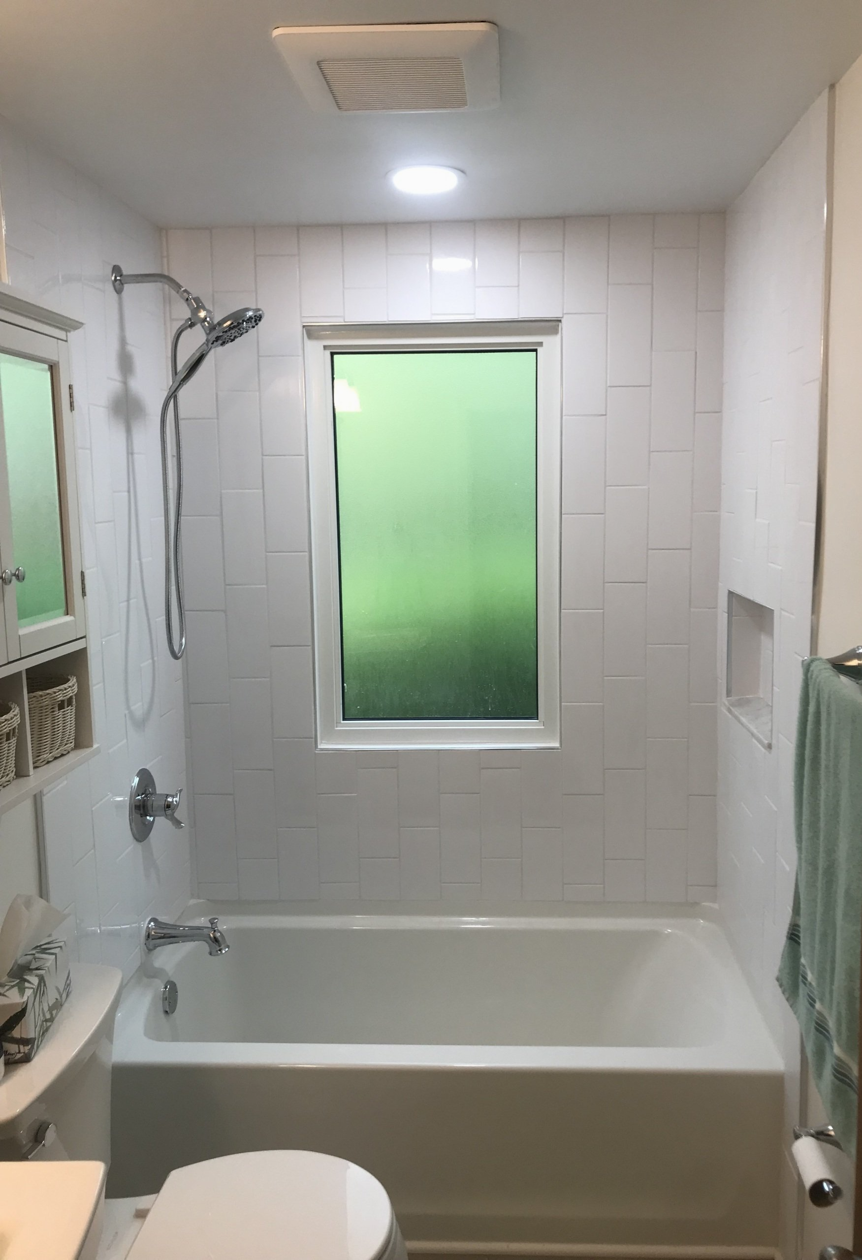 A bathroom with a tub , toilet , shower and window.