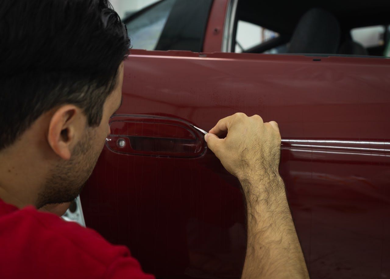 Person polishing a red car door with a cloth in a workshop
