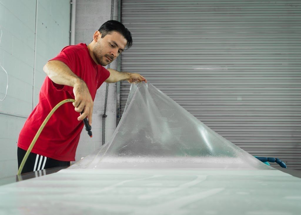Person in a red shirt peeling back a clear protective sheet from a car in a workshop