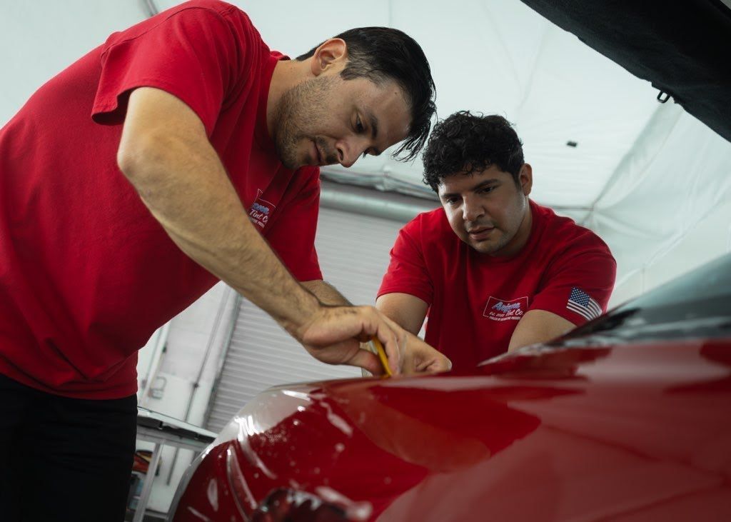 Two mechanics in red shirts inspect a red car in a garage
