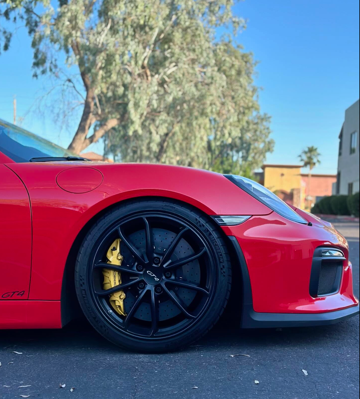 Red sports car close-up with black wheels and yellow brakes parked on a street.