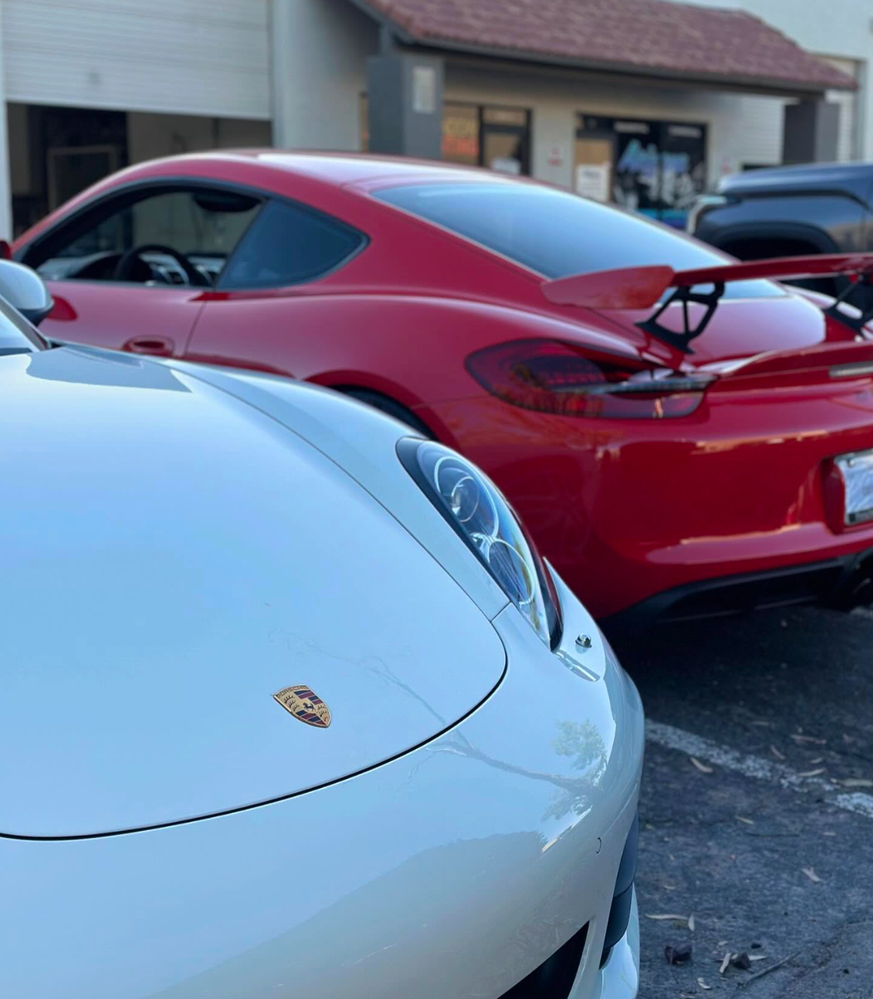 White Porsche in foreground and red sports car parked outside a building