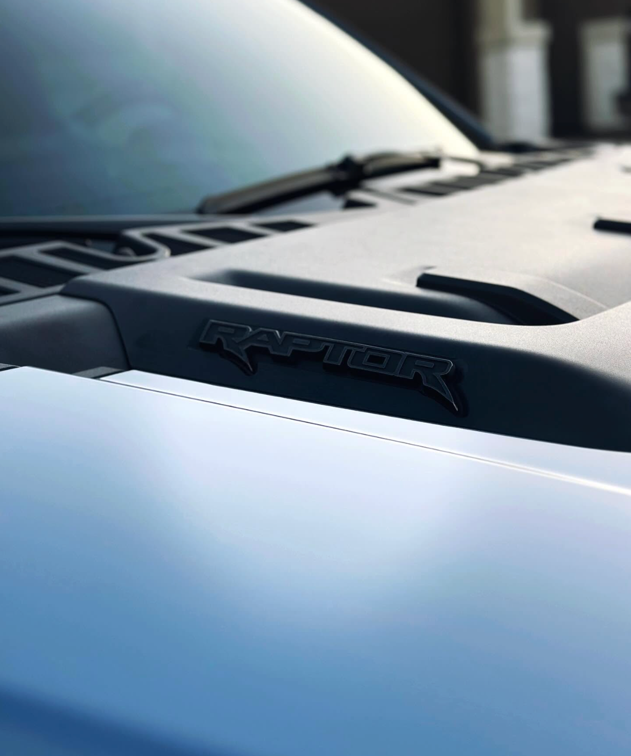 Close-up of a white Toyota Raptor hood and windshield in soft light