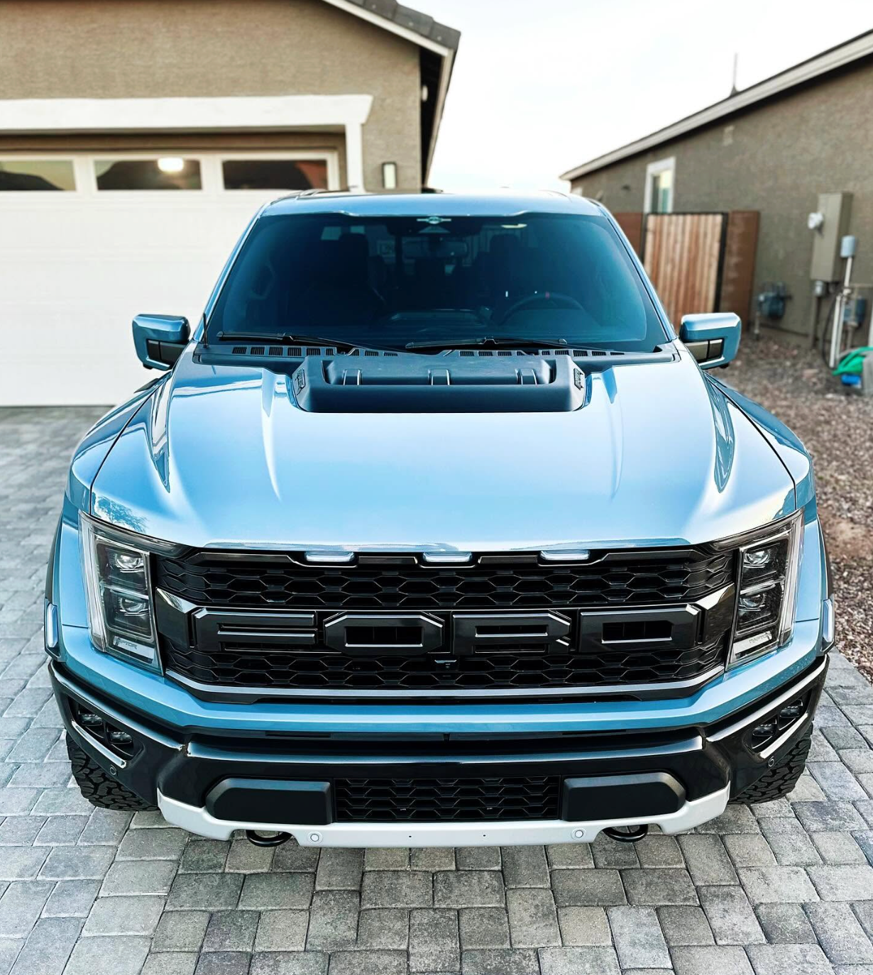 Blue pickup truck parked in a driveway in front of a house, front view.