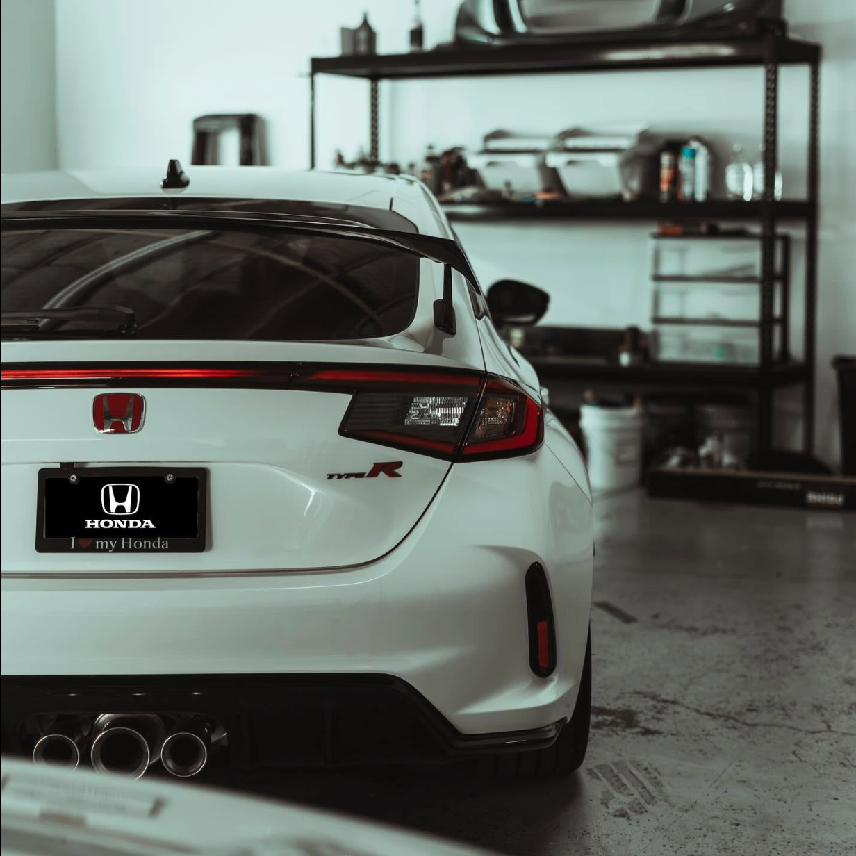 White Honda sports car parked in a garage, rear view with a black spoiler and exhausts