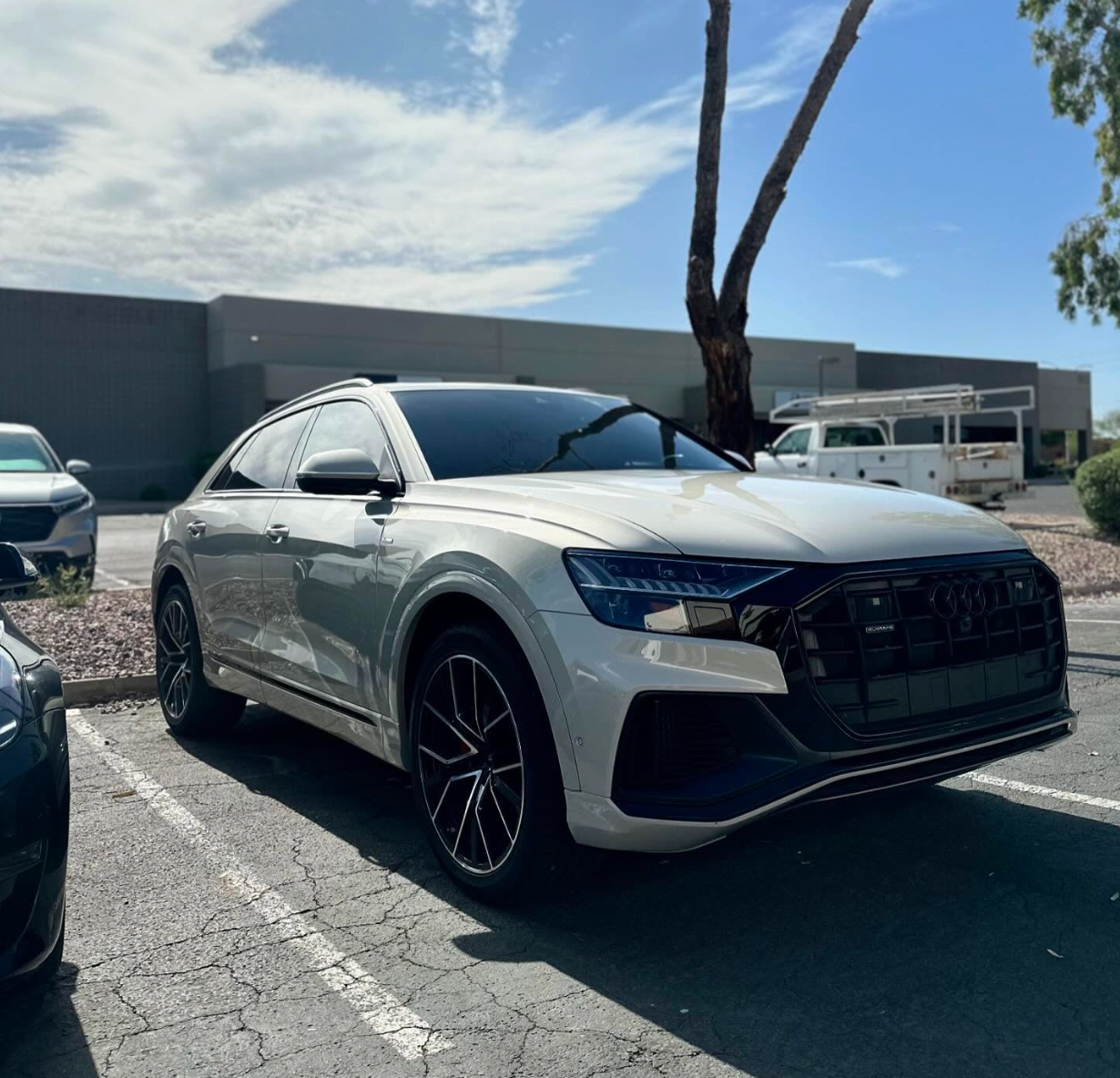 Silver Audi SUV parked outdoors in a sunny lot near a building and palm tree