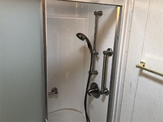 A shower stall with a shower head and handles in a bathroom.