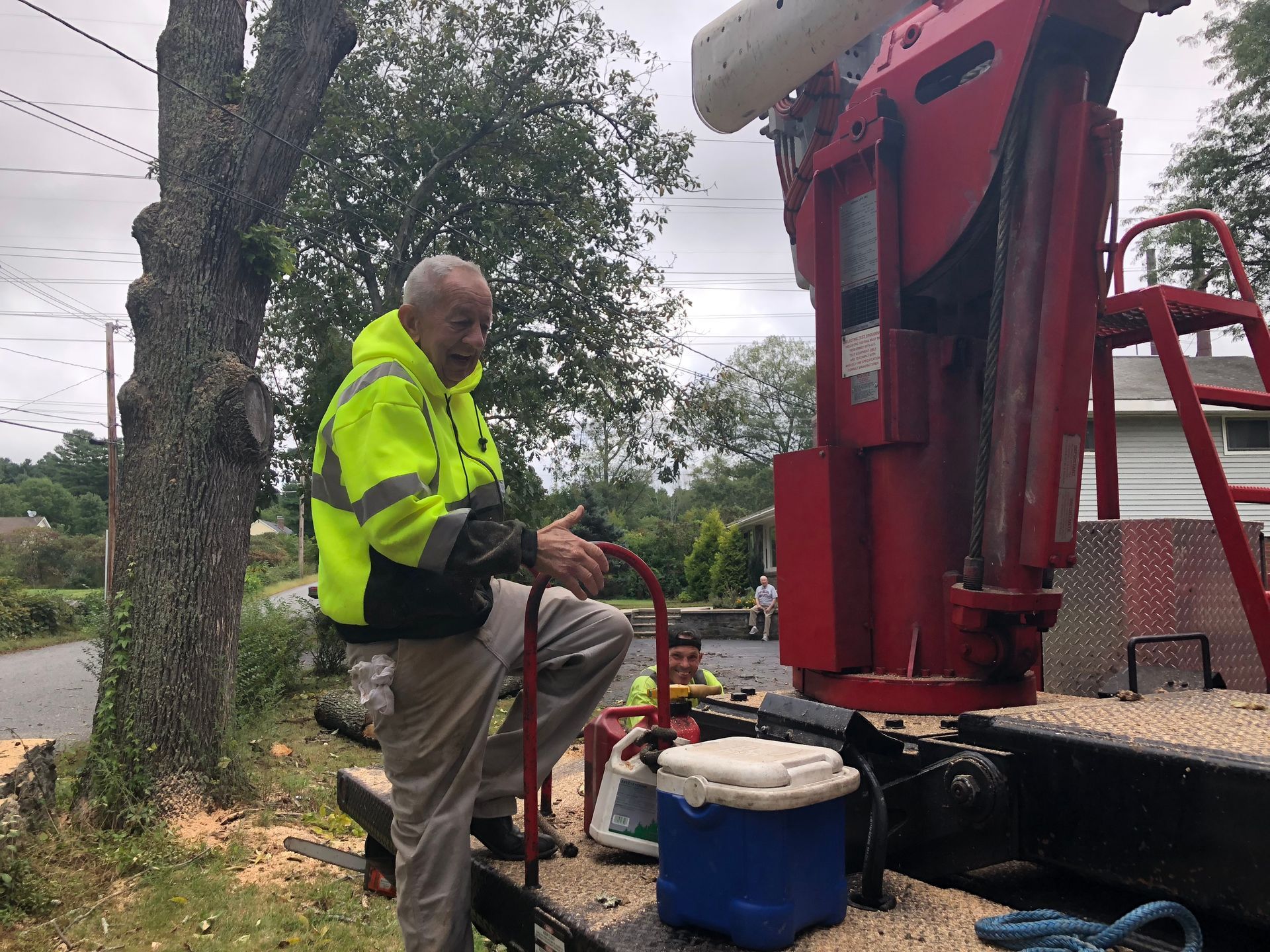 Man in safety vest operates tree trimming equipment outdoors.
