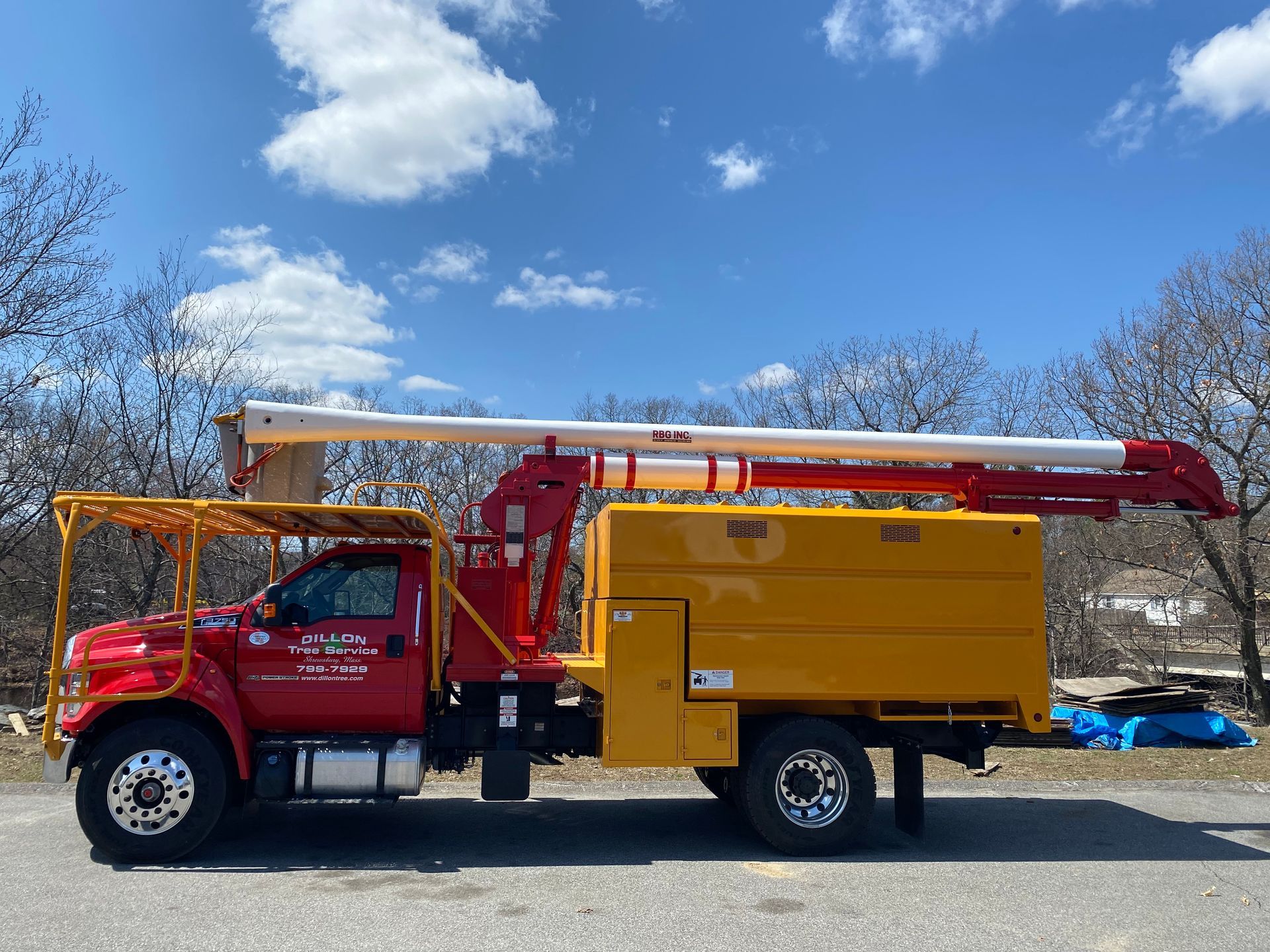 Red and yellow tree service truck with an extended boom under a blue sky.