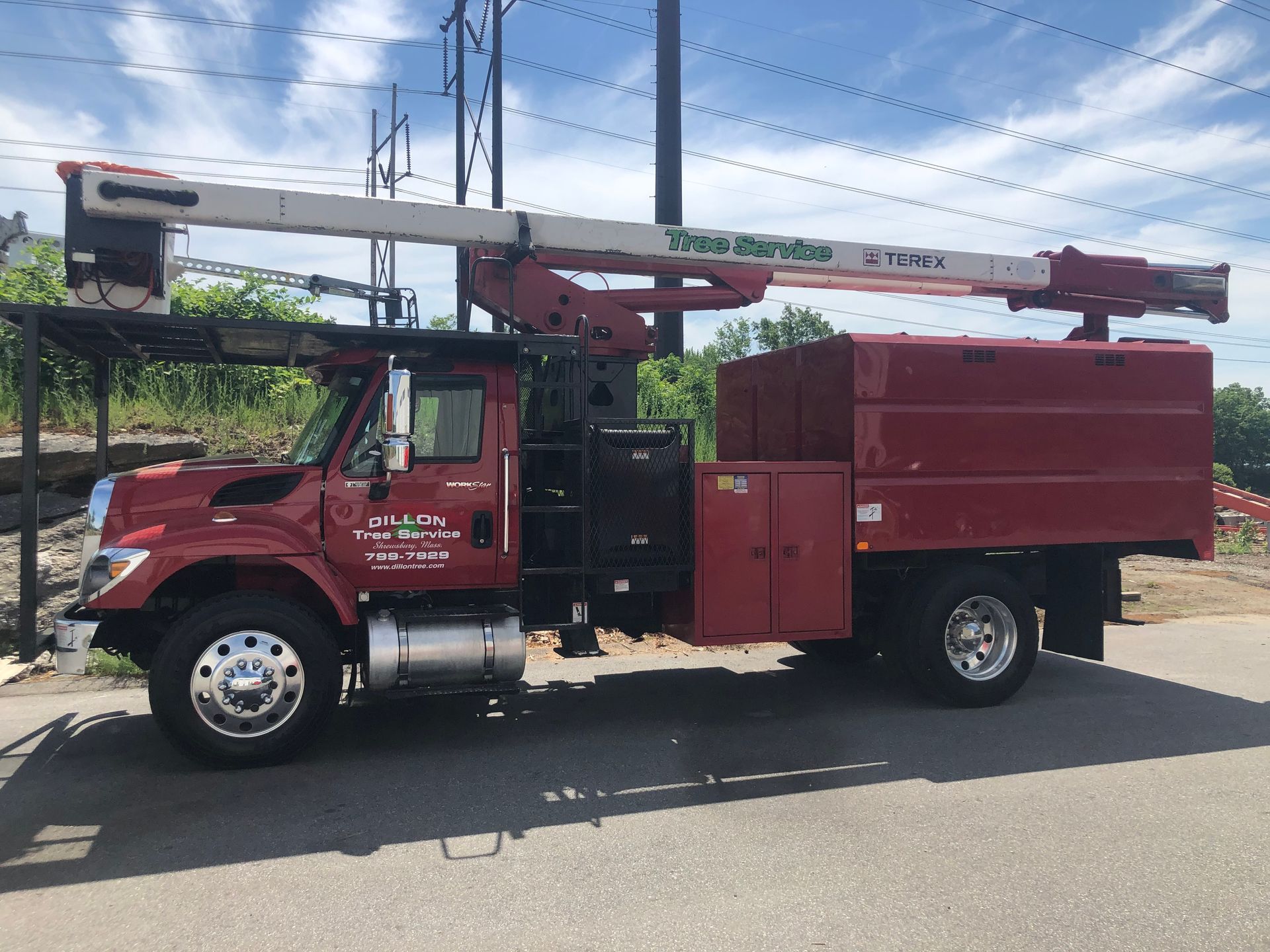 Red tree service truck with an extended boom, parked outdoors.