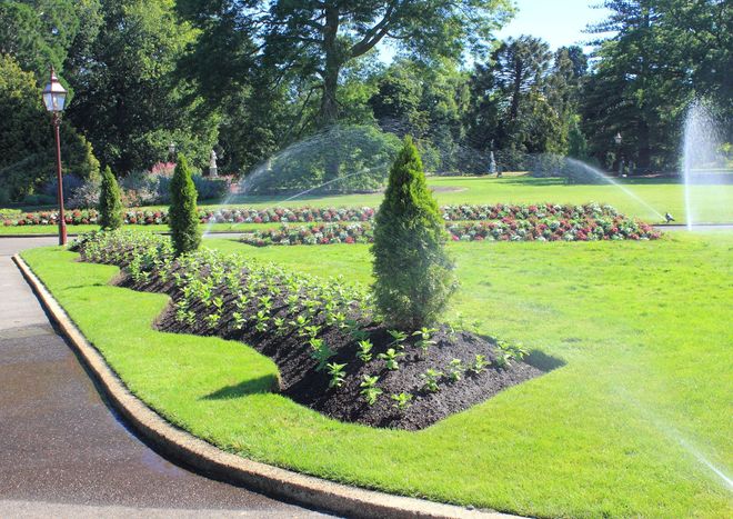 Formal garden with clipped shrubs, flower beds, and a fountain spraying water on a sunny day