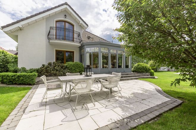 White house with glass sunroom and patio dining set on a lush green lawn