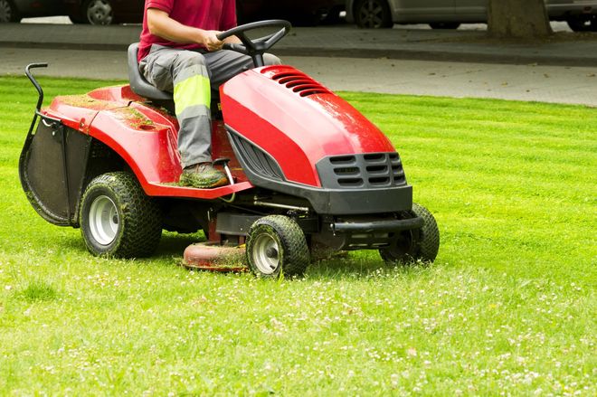 Person riding a red lawn tractor mowing a grassy yard