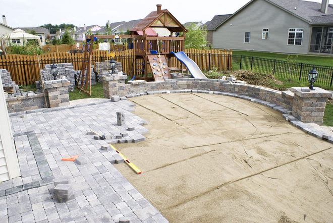 Backyard patio under construction with stone pavers, concrete slab, and wooden fence and houses in the background