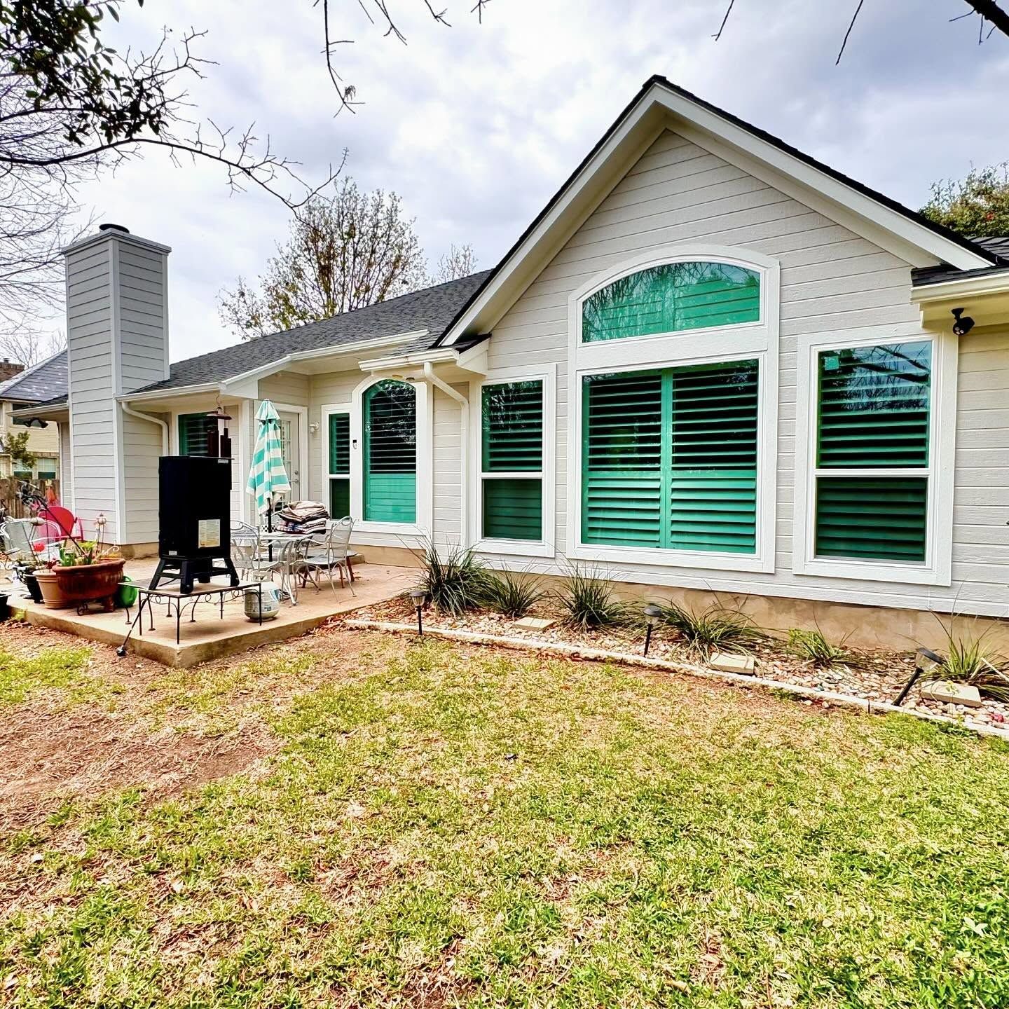 Bright interior room with three windows overlooking lush green trees. Brown floor, white trim, and a sofa.