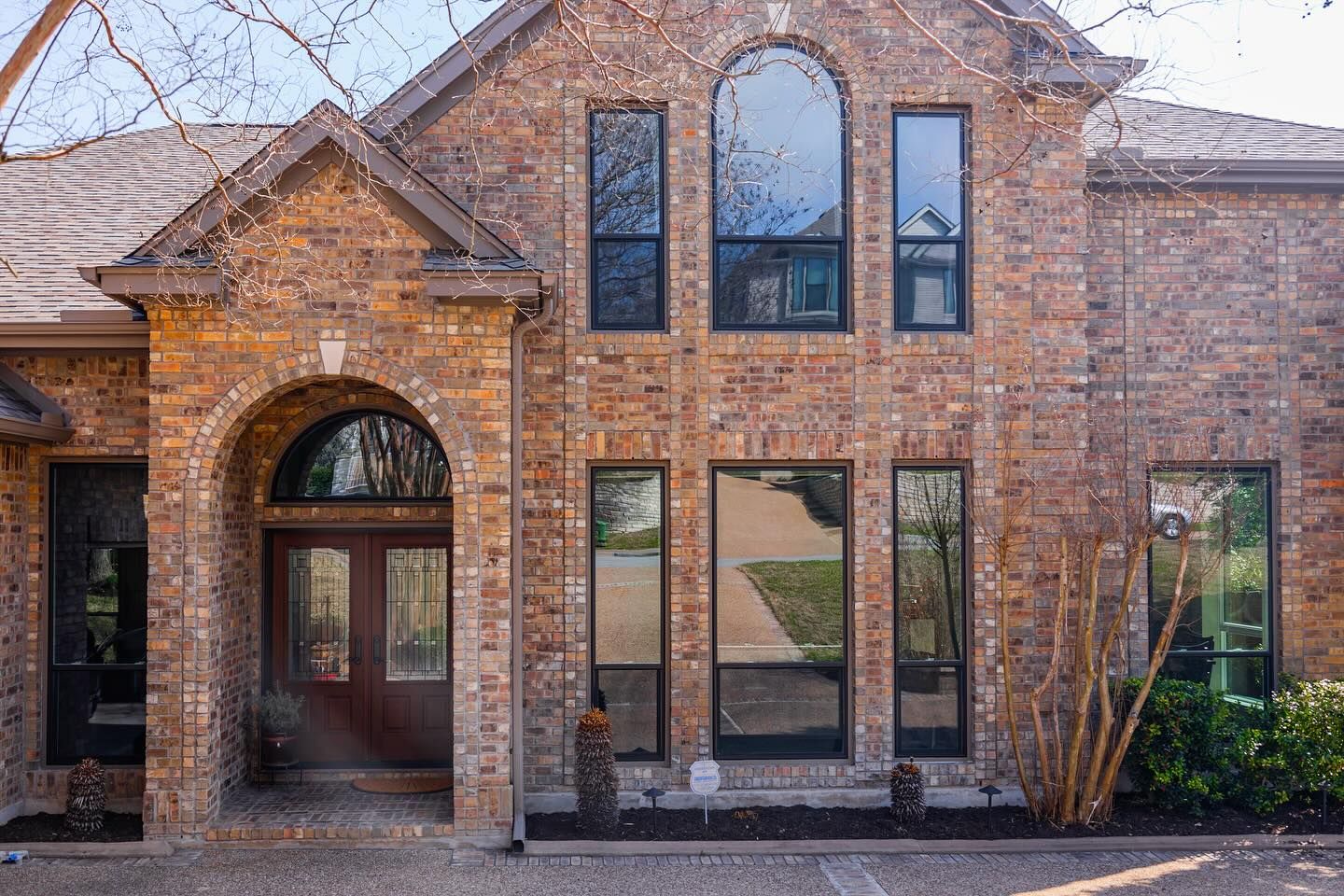 Before-and-after of a brick house with new windows and updated siding. Brown roof and green shutters.