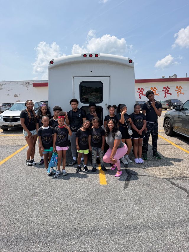 Group posing in front of a white vehicle outdoors on a sunny day