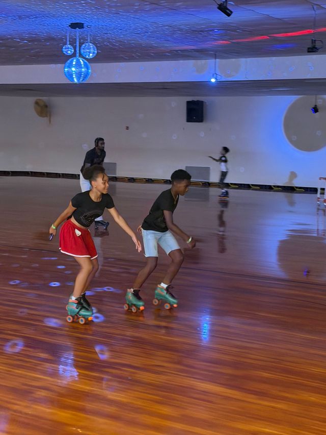 Two people roller skating in a rink with polished wooden floor and blue lighting