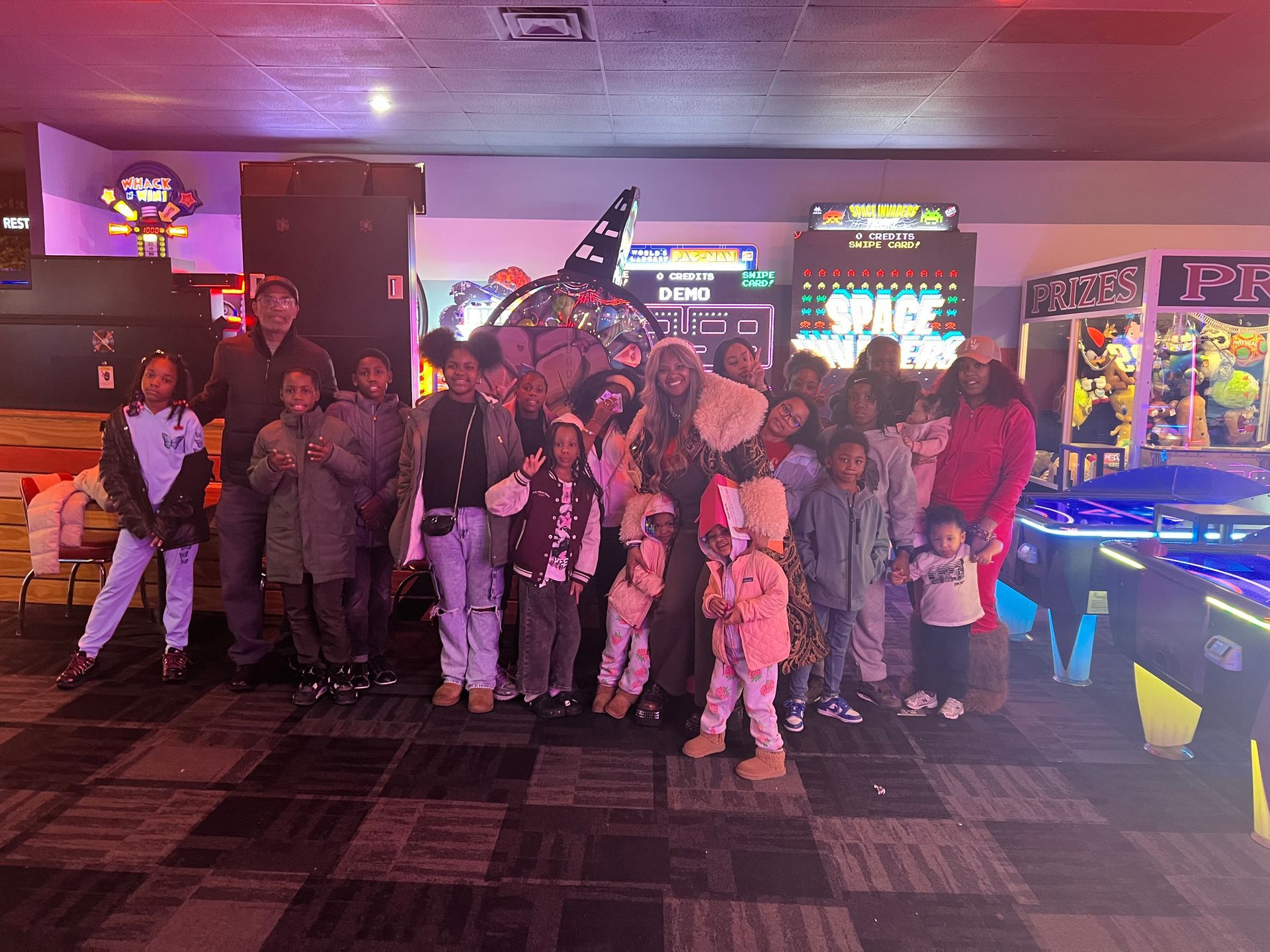 Group of people posing in a neon-lit arcade, with glowing game machines and colorful lights in the background.